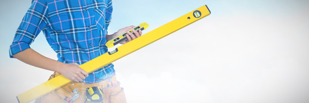 Female architect holding measuring equipment against grey background against blue sky with clouds