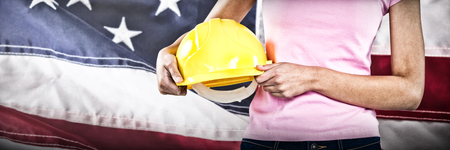 Woman holding hard hat against grey background against close-up of red and white american flag