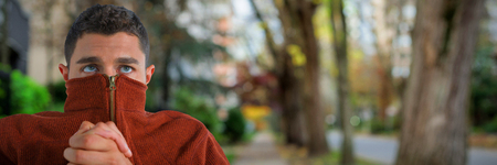 Man shivering from cold against footpath by trees in cityの写真素材