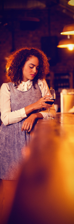 Thoughtful woman having red wine at counter in pubの写真素材
