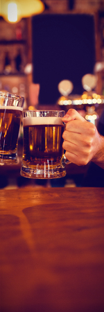 Two young men toasting their beer mugs in pubの写真素材