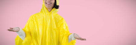 Woman in yellow raincoat gesturing to feel the rain against pink backgroundの写真素材