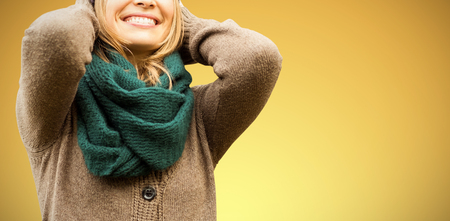 Beautiful blond woman with cap and scarf smiling against abstract yellow backgroundの写真素材