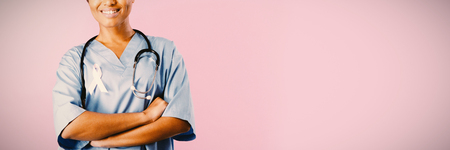 smiling nurse with crossed arms wearing pink ribbon om a pink backgroundの写真素材