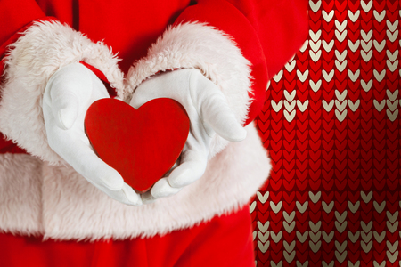 Santa Claus showing red heart shape against red seamless knitted patternの写真素材