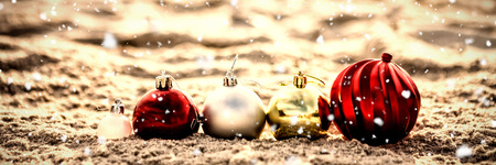 Snow falling against variety christmas baubles arranged on sandの写真素材