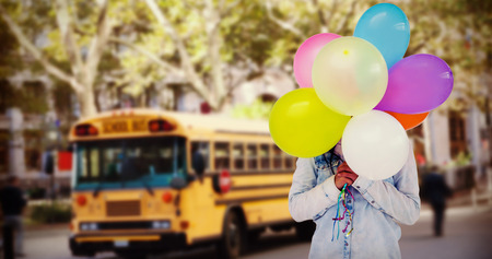 Woman hiding her face with bunch of colorful balloons  against schoolbus on ny streetの写真素材