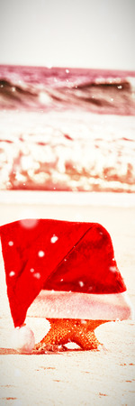 Snow falling against starfish with santa hat on beachの写真素材