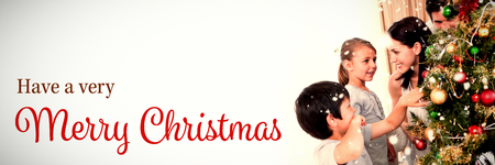 Christmas card against smiling family decorating a christmas tree with boublesの写真素材