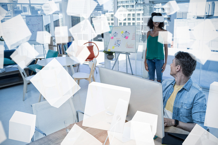 Man working on computer while female executive using virtual reality headset in officeの写真素材