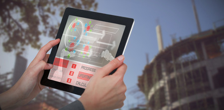 Cropped 3D image of businesswoman holding digital tablet against low angle view of construction siteの写真素材