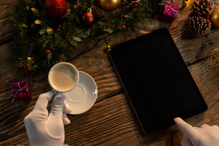 Santa Claus hands with coffee and tablet on a wooden table
