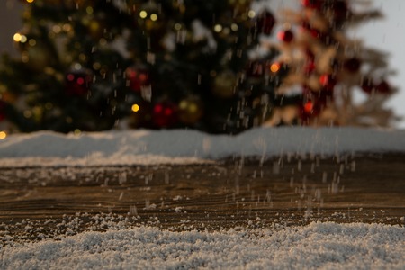 Wooden table with snow and unfocused Christmas treeの写真素材