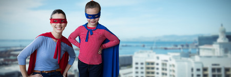 Mother and daughter pretending to be superhero against buildings by sea against skyの写真素材