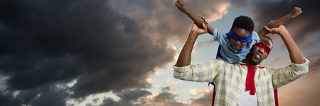 Father and son pretending to be superhero against blue and orange sky with cloudsの写真素材