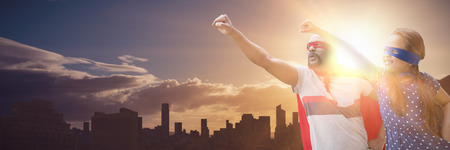 Father and daughter pretending to be superhero against picture of city by sunrise