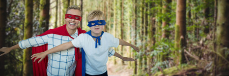 Mother and son pretending to be superhero against empty footpath amidst treesの写真素材