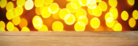 Composite image of wooden table against unfocused yellow christmas lightの写真素材
