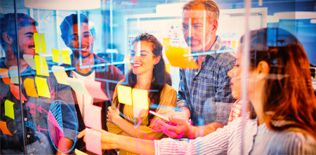 Creative business team looking at sticky notes on glass window in officeの写真素材