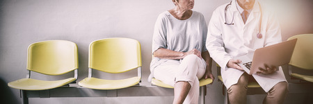 Doctor and patient discussing over laptop in hospital waiting roomの写真素材