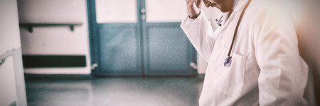 Sad doctor leaning against the wall in hospital corridorの写真素材
