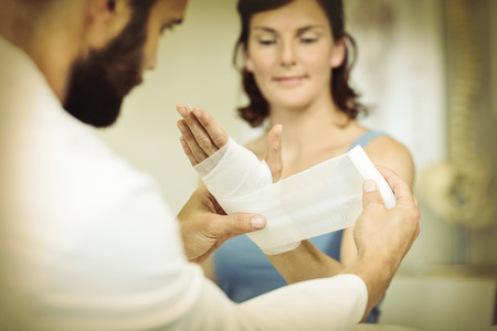 Physiotherapist putting bandage on injured hand of patient in clinicの写真素材