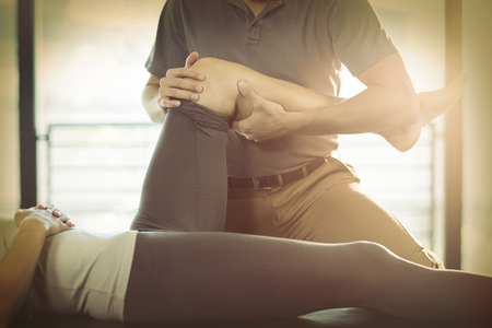 Physiotherapist giving knee therapy to a woman in clinicの写真素材