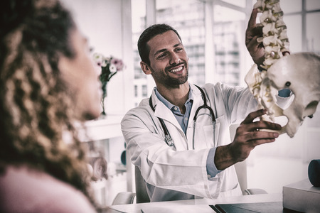 Physiotherapist explaining spine model to patient in clinicの写真素材
