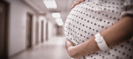 Mid section of pregnant woman standing in corridor of hospitalの写真素材