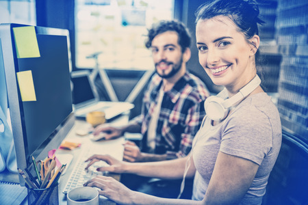 Portrait of happy businesswoman working with male colleague at computer desk in officeの写真素材