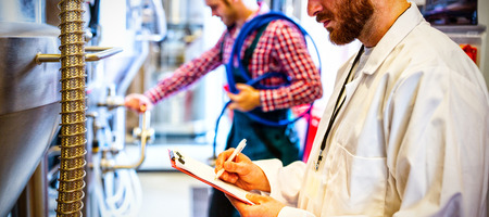 Maintenance workers examining brewery machine at brewery factoryの写真素材