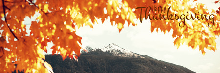 Illustration of happy thanksgiving day text greeting against leaves and snow capped mountainの写真素材