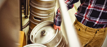Midsection of manufacturer holding kegs in brewery