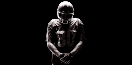 American football player standing with rugby helmat against black backgroundの写真素材