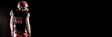 American football player standing with rugby helmet against black backgroundの写真素材