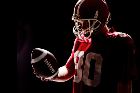 American football player with helmat looking at rugby ball against black backgroundの写真素材