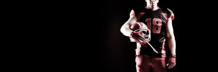 American football player holding rugby helmet against black backgroundの写真素材