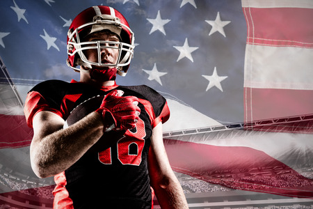 American football player in helmet holding rugby ball against close-up of an american flagの写真素材