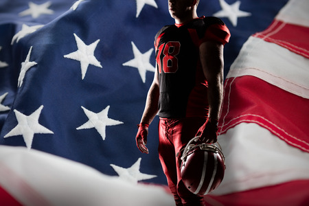 Volleyball player holding rugby helmet against full frame of american flagの写真素材