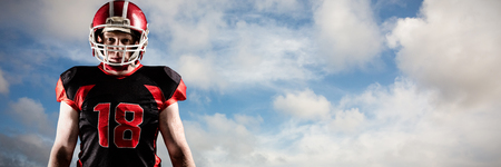 American football player standing in helmet against blue sky with white cloudsの写真素材