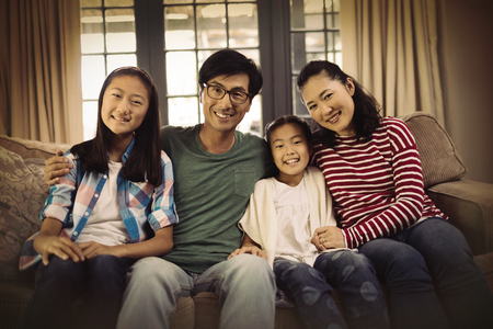 Portrait of smiling family relaxing on sofa in living room at homeの写真素材