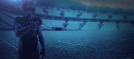 American football player in helmet holding rugby ball against digital image of rugby stadiumの写真素材
