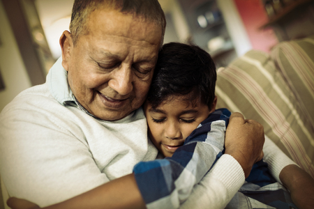 Boy embracing grandfather while sitting on sofa at homeの写真素材