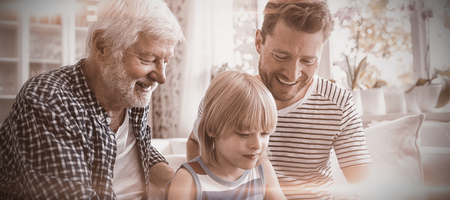 Boy using digital tablet with his father and grandfather in living room at homeの写真素材