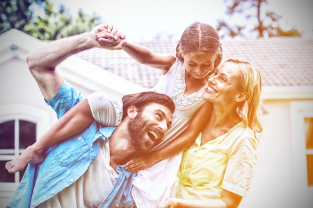 Father carrying daughter on shoulder besides woman in yardの写真素材