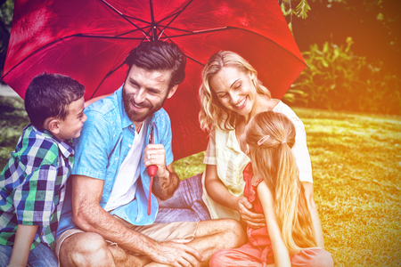 Happy family with umbrella sitting on grass at yardの写真素材