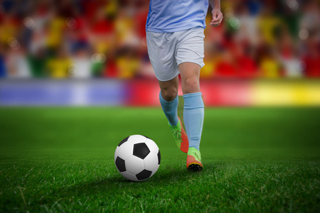 Male soccer player playing football against soccer stadiumの写真素材