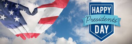 USA flag painted on hands making heart shape against blue sky with white cloudsの写真素材