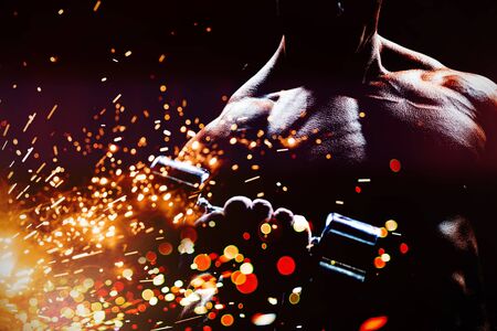 Concentrated bodybuilder lifting dumbbell against firework bursting sparkle backgroundの写真素材