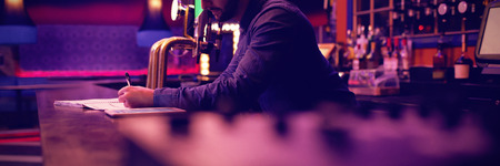 Bartender maintaining records at the counter in barの写真素材